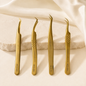 Essira Luxe Gold Series four-piece tweezer collection on a luxury cream background